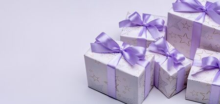 Gift boxes in elegant paper with lilac ribbons, on lilac background. Happy Holidays. Copy space.の写真素材