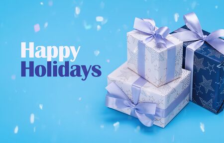 Gift boxes with patterns, lilac ribbon with bow. Happy Holidays. Copy space for your text on blue...