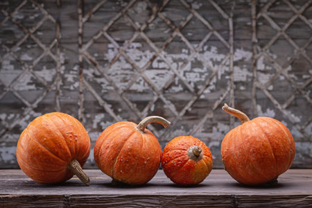 Decorative orange pumpkins on dark wooden table. Old gray background with geometric pattern, studio shot.の写真素材