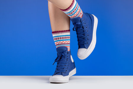 Woman's legs in blue sneakers and colored socks with ornaments, blue background. Sports and...