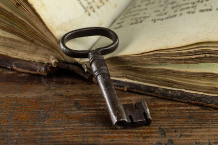An old metal key lies on the pages of an open antique book. On a dark wood surface, retro objects.の写真素材