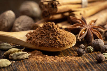 Wooden spoon with ground cinnamon and cinnamon rolls. Whole nutmegs, cordamom, anise, allspice peas. A set of spices on a brown table.の写真素材