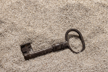 An old metal key on the coarse sea sand. Background and wallpaper concept, copy space.の写真素材
