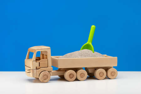 A miniature wooden toy cart filled with sand with a green shovel in it. Fun for boys, close-up, blue background.の写真素材