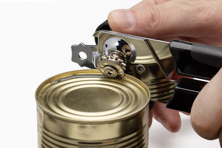 In men's hands a can opener opening a can of food. Kitchen utensils.の写真素材