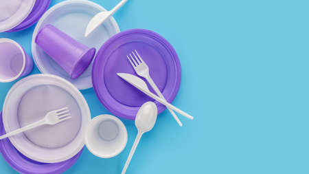 A set of disposable, lilac and white, plastic utensils. Blue background, copy space. The concept of...