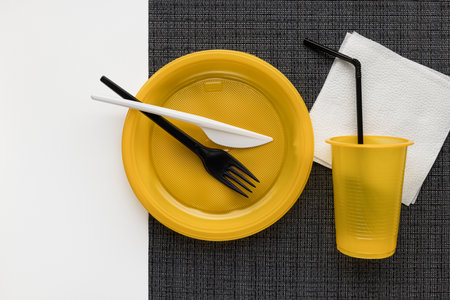 Yellow crockery on a black and white background. Still life with disposable tableware. plastic recycling.の写真素材