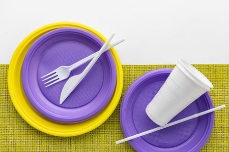 A set of multi-colored disposable tableware on a white background, a yellow plastic napkin, top view.の写真素材