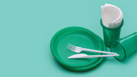 Disposable green plates, glasses for drinks and cutlery on a green background, paper napkins. plastic recycling.の写真素材