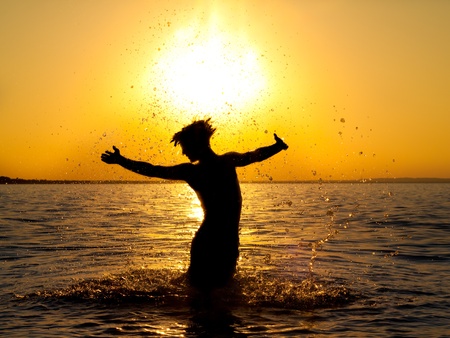Swimmer jumping out of sea water on golden sunsetの写真素材
