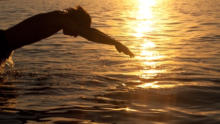 Swimmer jumping out of sea water on warm sunriseの写真素材
