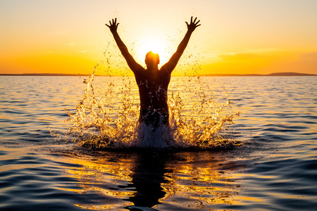 Swimmer jumping out of sea water at warm sunriseの写真素材