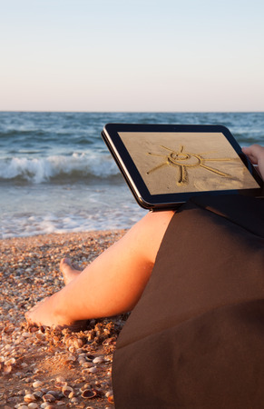 back view of a young girl towards her tablet with sun  picture on beachの写真素材