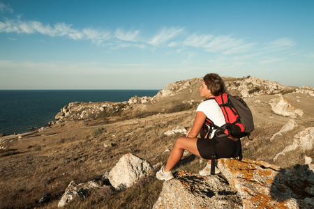 woman hiker with backpack sits on seaside mountain rockの写真素材