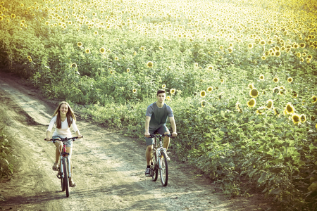 Two happy teen cyclist in sunflower field riding bicycle. Healthy lifestyle conceptの写真素材