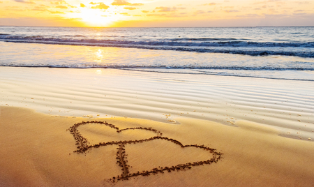 Valentines day on sunny beach. Two hearts drawn in sand, love conceptの写真素材