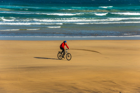 Sporty young man ride bicycle on sand Famara beach. Lanzarote Canary Islandの写真素材