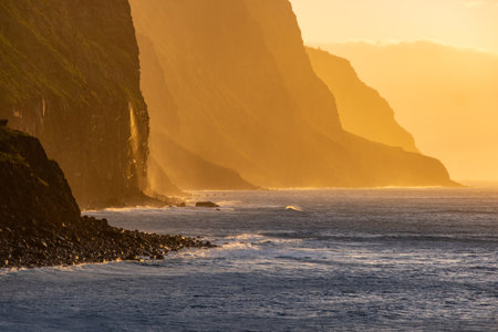 Volcanic rock cliffs Achadas da Cruz in backlit sunlight. Waves of the Atlantic Ocean. Beautiful sunset seascape of the resort island of Madeira, Portugalの写真素材