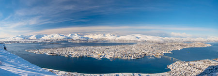 Aerial Panorama of norwegian city of Tromso in the winter. Snowy roofs, embankment near the port and fishing ships, Sunny winter day.の写真素材
