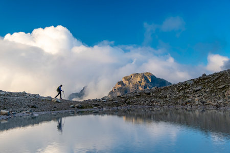 Aerial view to woman with backpack hiking near lake on mountain top in Swiss alps enjoying sunny...