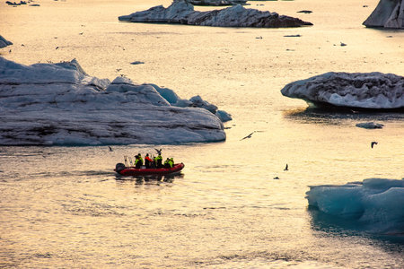 Group wearing bright jackets explores icebergs on an inflatable boat in a serene water setting...