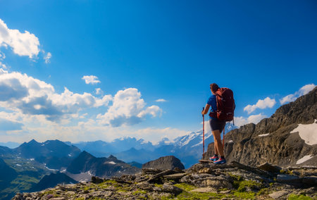 A lone hiker pauses on a rocky peak, gazing at the breathtaking mountainous terrain below. Sporty...