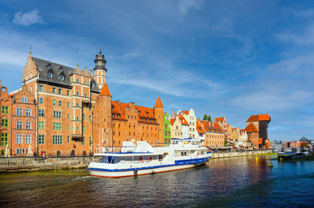Scenic view of two boats navigating the Motlawa River alongside historic colorful buildings in Gdansk, Poland. Bright blue skies enhance this vibrant European cityscapeの写真素材