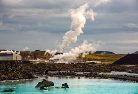 A geothermal power station set against the striking backdrop of Blue Lagoon in Iceland, with steam billowing from the facility and turquoise waters in the foreground.の写真素材
