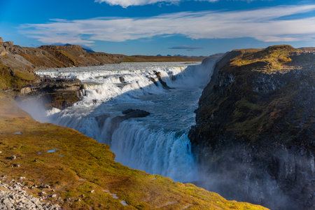 Gullfoss waterfall in Iceland showcases powerful cascades flowing into a canyon. Visitors admire the...