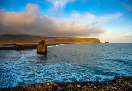 Kirkjufjara beach showcases black sand and unique rock formations under a vibrant sunset. The...