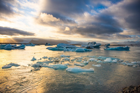 Icebergs float in Icelands glacier lagoon, reflecting the warm colors of sunset. Birds fly above, adding life to the tranquil scene. This location is a must-see for nature enthusiasts.の写真素材