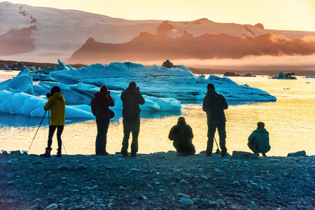 Tourists admire the stunning sunset over Icelands Glacier Lagoon, surrounded by large icebergs. The...