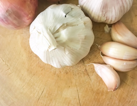 Onion and garlic on wooden chopping board.