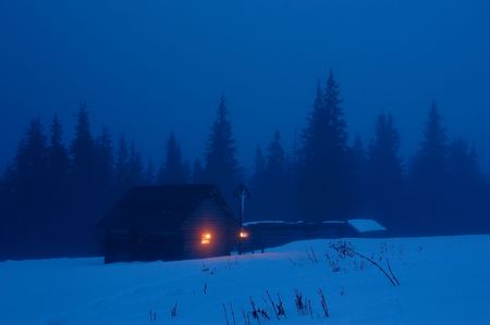 High-mountainous small house in the Ukrainian Carpathians. Winter evening, on a cross with Jesus burns a candleの写真素材