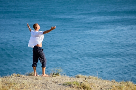 Young man enjoying the sea breeze while standing on a rockの写真素材