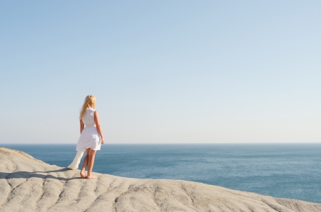 Beautiful girl in white dress standing on a rock and looking at the seaの写真素材