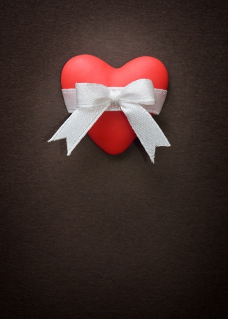 Red heart with a white bow on a background of brown paperの写真素材
