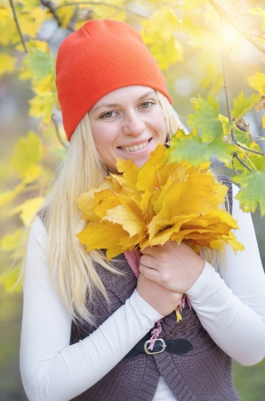 Happy young blond woman smiling and holding a bouquet of yellow autumn leavesの写真素材