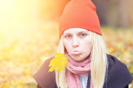 Blonde girl in orange hat with yellow autumn leafの写真素材