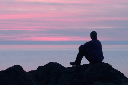 Evening at the seaside  Guy sits on a rock by the sea and looking at sunsetの写真素材