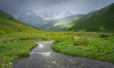Rain in the mountains  Rainbow over the river  Mountain landscape on a rainy summer day  Caucasus, Georgia, Svaneti  View at the foot of the mountain Shkharaの写真素材