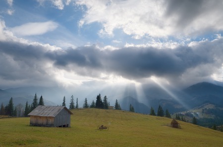 Rural landscape with beautiful sun rays through the clouds  Wooden hut in the mountainsの写真素材