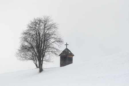 Winter landscape. Wooden chapel and a tree on a hill. The village is in the mountains. Carpathians, Ukraine, Europeの写真素材