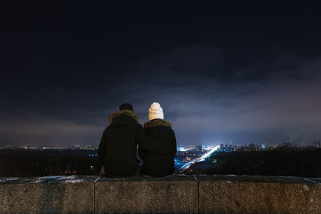 Loving couple looking at city night. Man and woman sitting in an embrace