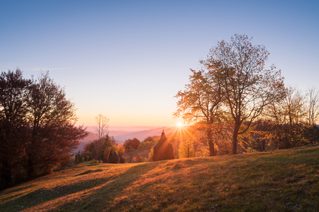 Autumn landscape in a mountain village. Beautiful sunset with a warm glow. Stacks dry hay in a meadow. Subsistence agriculture. Carpathian, Ukraine, Europe. HDR and color toningの写真素材