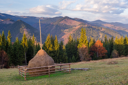 Autumn landscape at sunset. Haystack on the meadow in a mountain village. Sky with beautiful clouds. Carpathians, Ukraine, Europeの写真素材