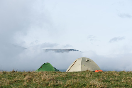 Two tourist tents on a hill. Hiking in the mountains. Autumn landscape with low clouds