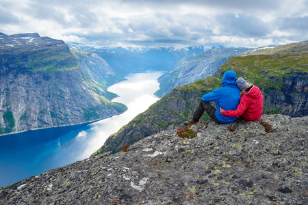 Couple sits on rock and looks at mountains near Trolltunga. Popular tourist attraction. Ringedalsvatnet - lake in the municipality of Odda in Hordaland county, Norwayの写真素材