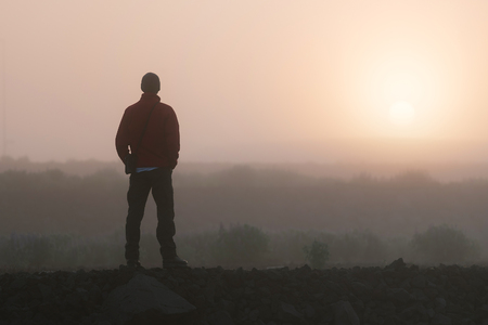 Man thinks looking at the rising sun. Morning landscape with fogの写真素材