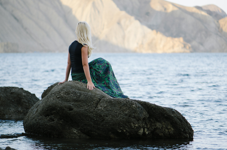 European blonde woman is resting on the seashore. Summer landscape with sea and mountain views. Sunny weather in the morningの写真素材